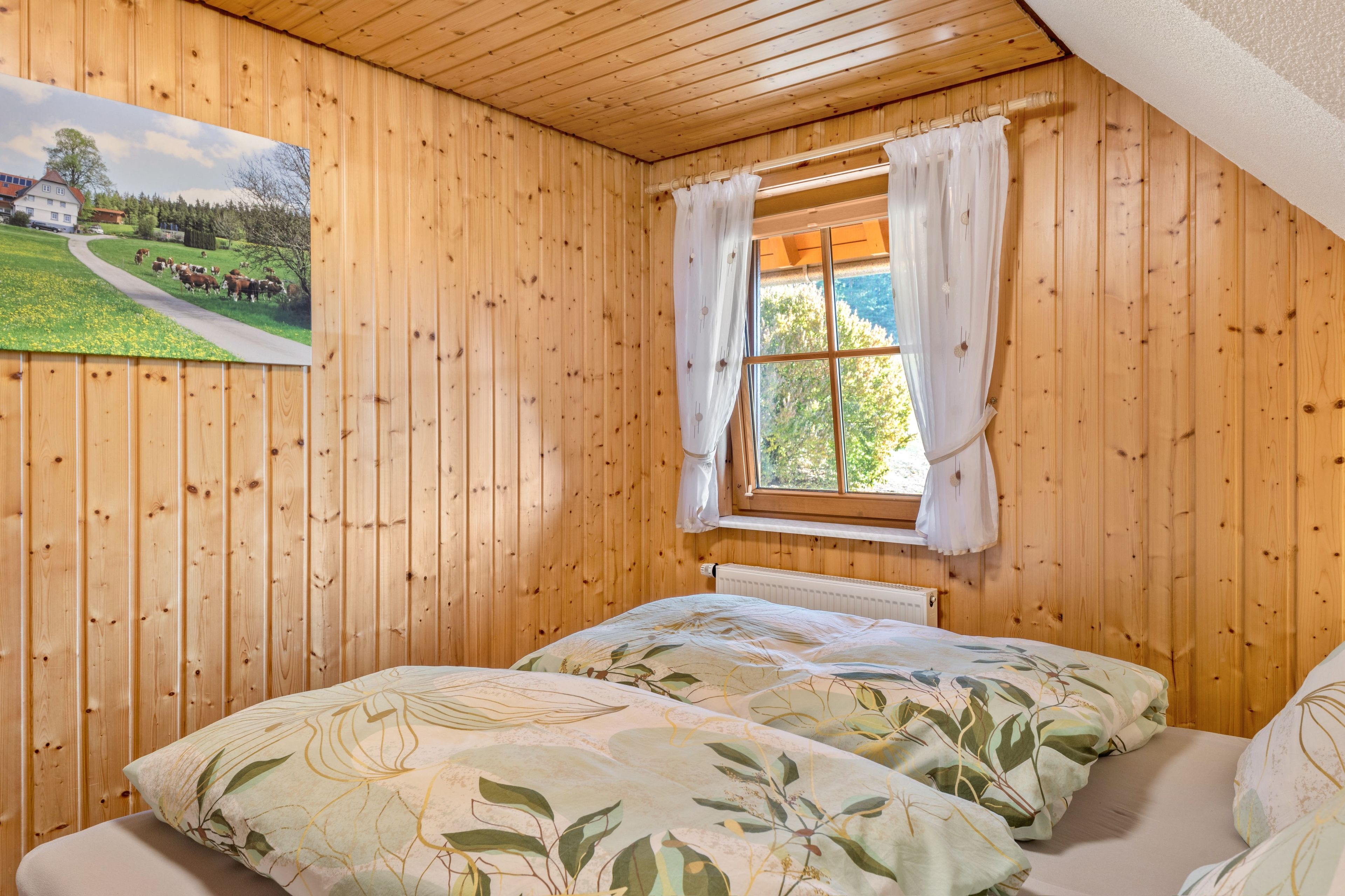 Ein Zimmer mit Holzwänden, einem Bett, einem Vorhangfenster und einem Bild an der Wand.