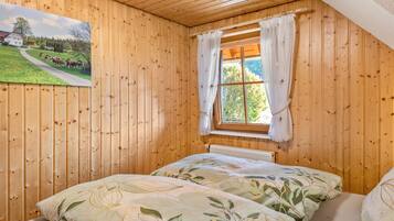 A wooden-paneled room with a bed, a window with curtains, and a painting on the wall.