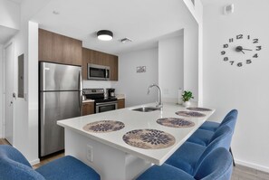 A modern kitchen with a stainless steel refrigerator, microwave, and oven, a sink, and a clock on the wall. - Steps to Marketplace • Near Cruise Terminal & Airport (Miami)