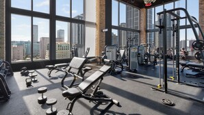 Et fitnesscenter med store vinduer, træningsudstyr og udsigt over byen.