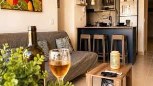 Ett vardagsrum med en soffa, ett soffbord med ett glas vin på, en krukväxt och en tavla på väggen.