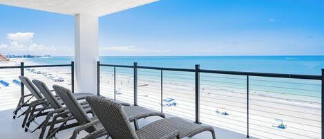 Un balcon avec des fauteuils en osier et une table donnant sur une plage aux eaux d’un bleu limpide.