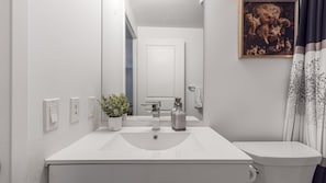 A bathroom with a white sink, a mirror, a potted plant, a toilet, and a painting on the wall. - Dundas Square Gardens (Toronto)