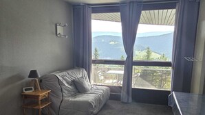Quarto com cama, mesa pequena, cadeira, escrivaninha e vista para o exterior.