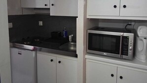 Cozinha compacta com armários brancos, micro-ondas, cafeteira e máquina de lavar louça.
