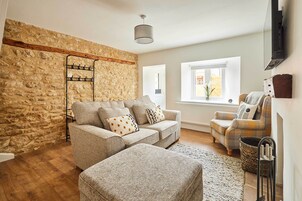Un salón acogedor con pared de piedra, viga de madera, sofá, alfombra estampada y televisor.