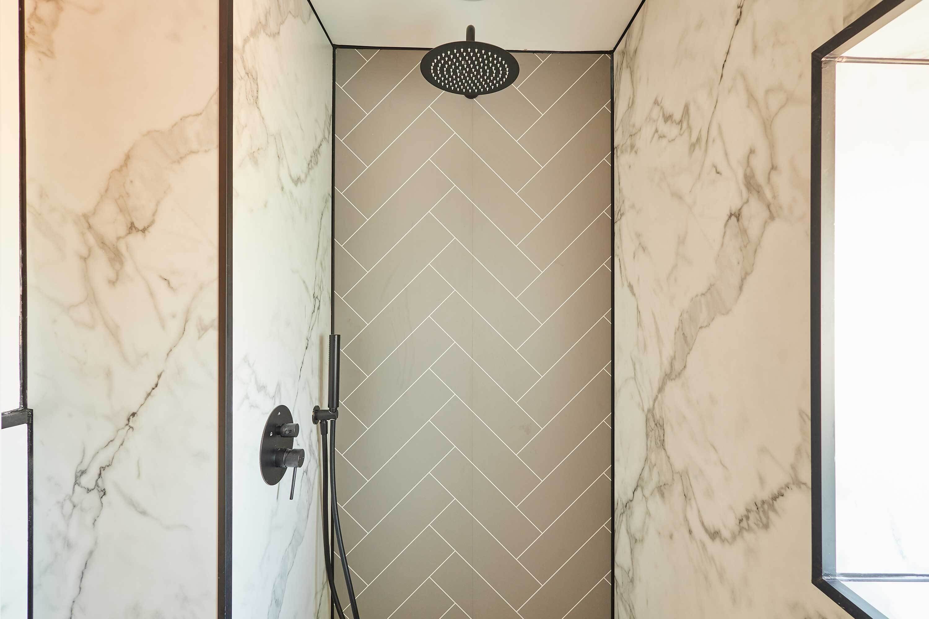 Un baño con pared de diseño espiga, ducha con rociador redondo y panel de control visible.