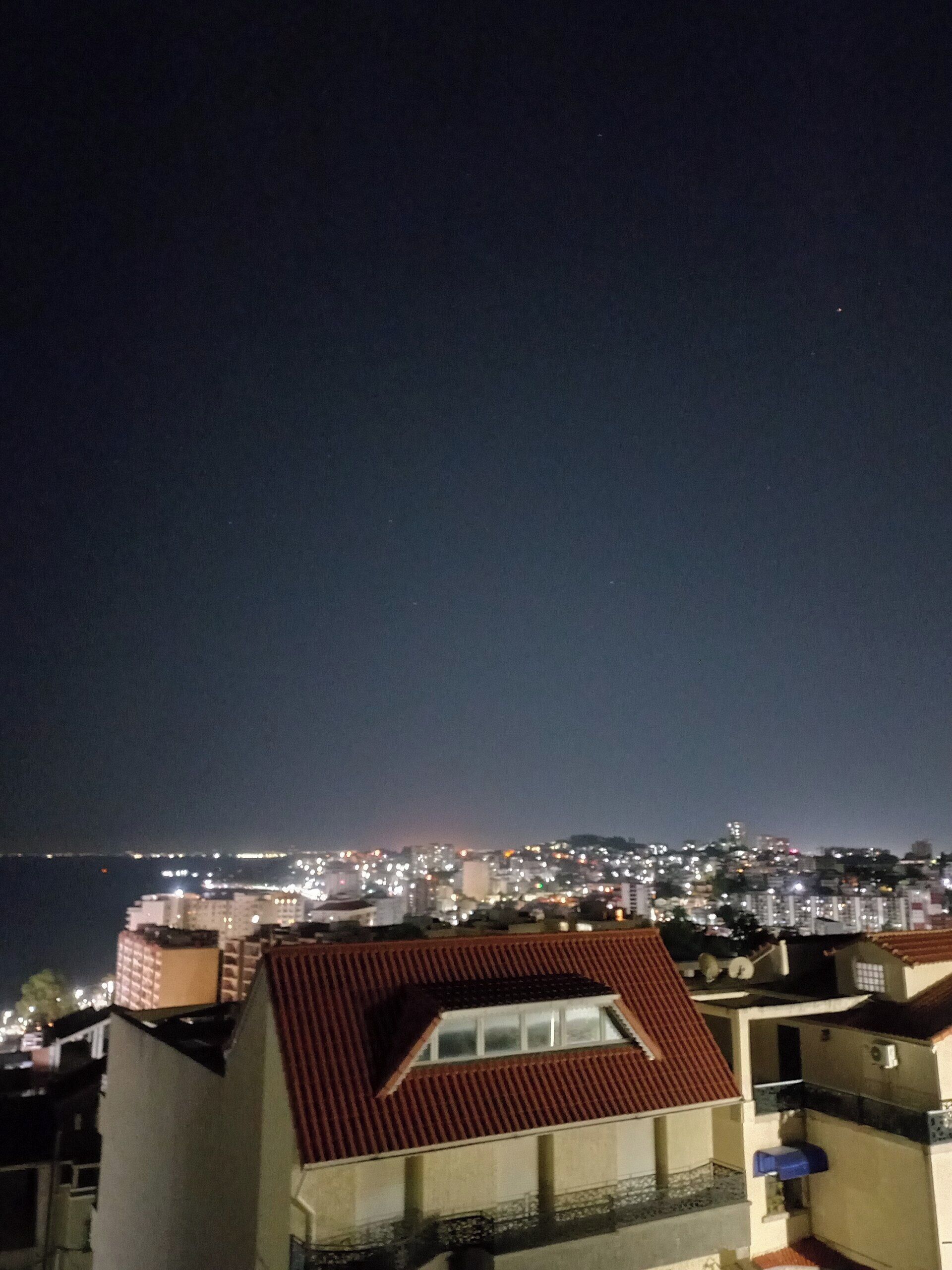 Une vue nocturne d’une ville côtière, avec ses bâtiments et une étendue d’eau.