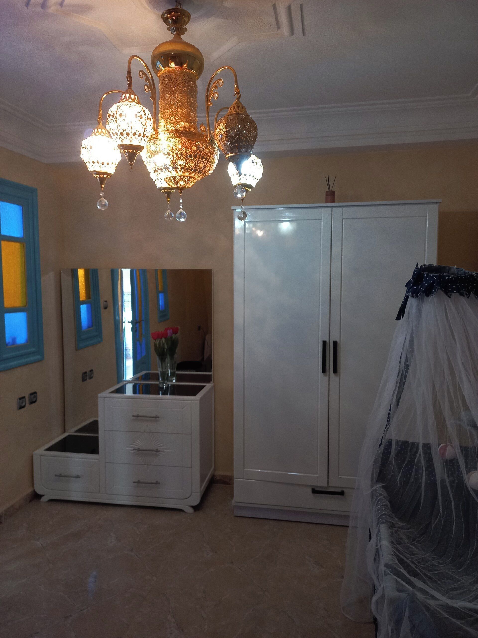 Quarto com lustre, guarda-roupa, penteadeira e cama com dossel.
