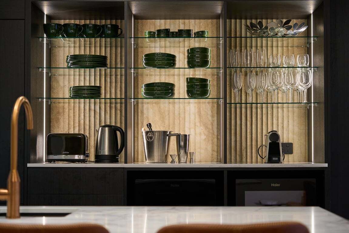 A kitchen with glass shelves displaying green plates, glasses, and a kettle.