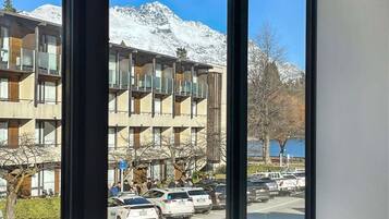 Un immeuble à plusieurs étages, avec un parking devant, une enseigne bleue et, en arrière-plan, des montagnes enneigées.