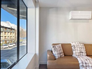 A modern room with a large window, a brown leather sofa, and a white air conditioning unit.