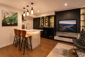 A modern kitchen with a central island, bar stools, a large flat-screen TV, and a fireplace.