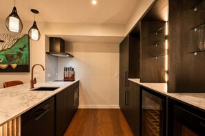 A modern kitchen with dark cabinetry, a marble countertop, and pendant lighting.
