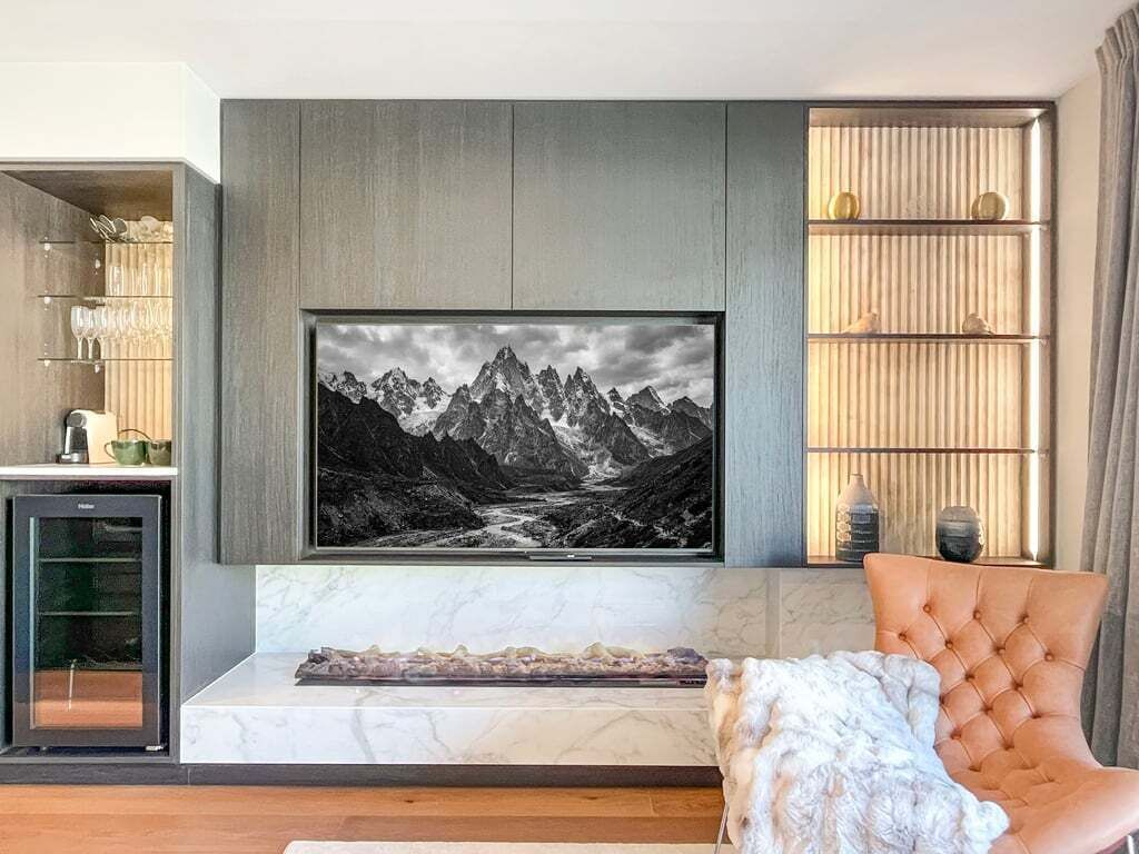 Una sala moderna con un amplio cuadro de un paisaje montañoso, un aparador de vidrio y un sillón cómodo.