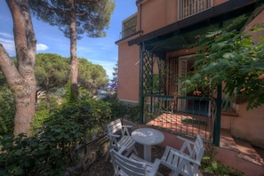 A courtyard with a table and chairs, surrounded by trees and a building with a balcony. - Il Pulcino della Pavona - sea view and garden (Monterosso al Mare)