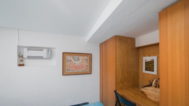 Ein Zimmer mit einem Bett, einem Schreibtisch, einem Stuhl, einer Wandklimaanlage und zwei gerahmten Bildern.