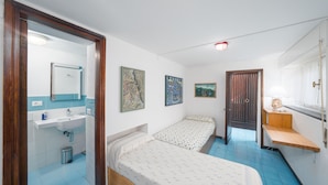 Ein Schlafzimmer mit zwei Betten, einem Badezimmer mit Waschbecken und einem Fenster mit Vorhängen.