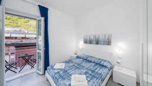 A bedroom with a bed, a nightstand, a wall-mounted lamp, a window with curtains, and a balcony with a table and chairs. - Charlie 89 Modern Apt with A/C in the center (Monterosso al Mare)