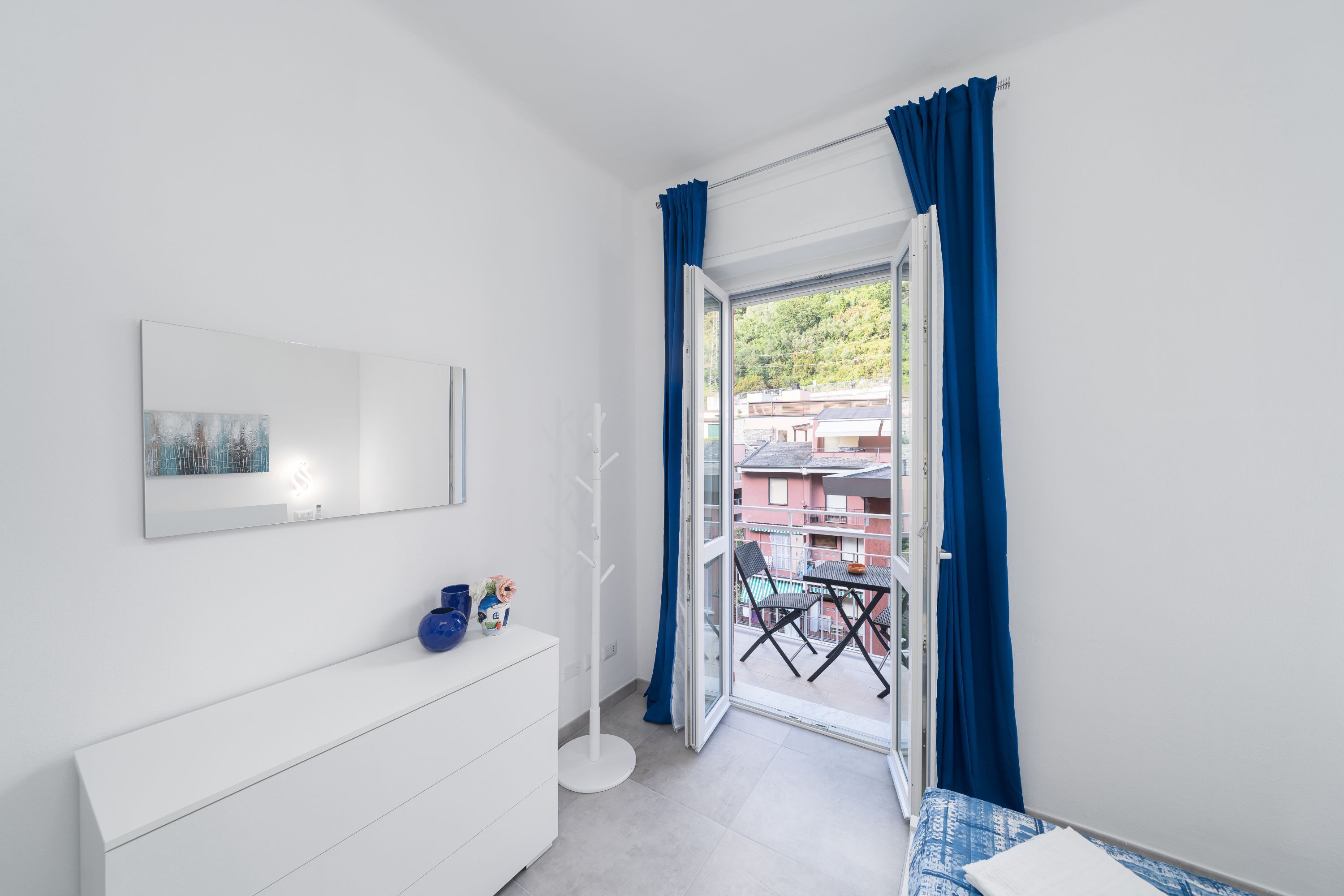 A modern bedroom with a white dresser, a glass door leading to a balcony, and a framed picture on the wall.