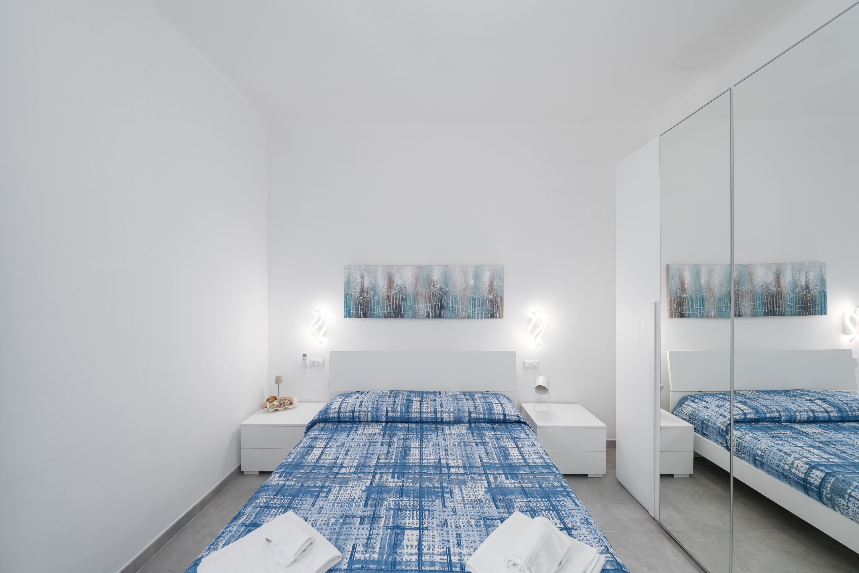 Ein modernes Hotelzimmer mit einem großen Bett, Nachttischen, einem Spiegel und Bildern an der Wand.