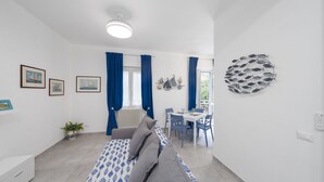 A modern room with a bed, a dining table, chairs, a radiator, and a wall art piece. - Charlie 89 Modern Apt with A/C in the center (Monterosso al Mare)