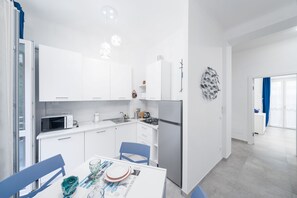 Een moderne keuken met witte kasten, een eettafel met stoelen, een koelkast en een magnetron.