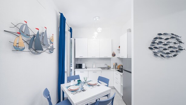 A modern kitchen with white cabinets, a dining table with blue chairs, and decorative wall art. - Charlie 89 Modern Apt with A/C in the center (Monterosso al Mare)