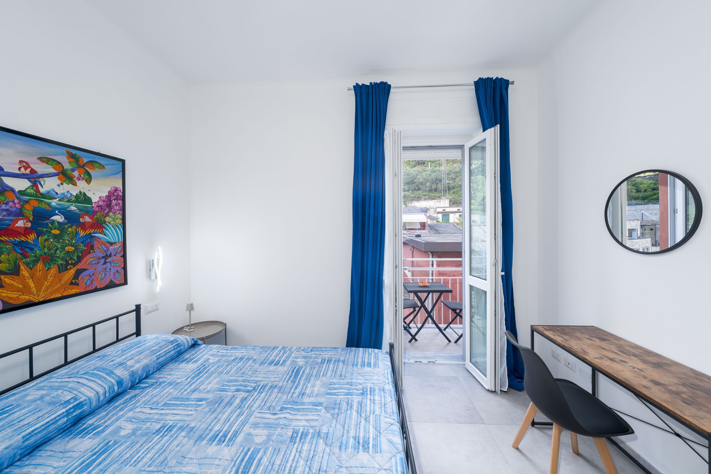 Une chambre à coucher avec un lit, un bureau, une chaise, un tableau et une vue sur l’extérieur.
