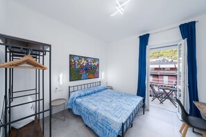 Slaapkamer met een bed, een kledingrek, een schilderij, een klein tafeltje en een balkon met stoelen.