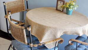 A wicker chair with a blue cushion, a round table with a beige tablecloth, and a small blue pot with yellow flowers. - Modern loft 5 minutes from Geribá with a balcony, grill, and pool—pets welcome! (Armação dos Búzios)