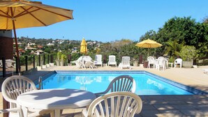 A swimming pool with white chairs and tables, surrounded by umbrellas. - Modern loft 5 minutes from Geribá with a balcony, grill, and pool—pets welcome! (Armação dos Búzios)