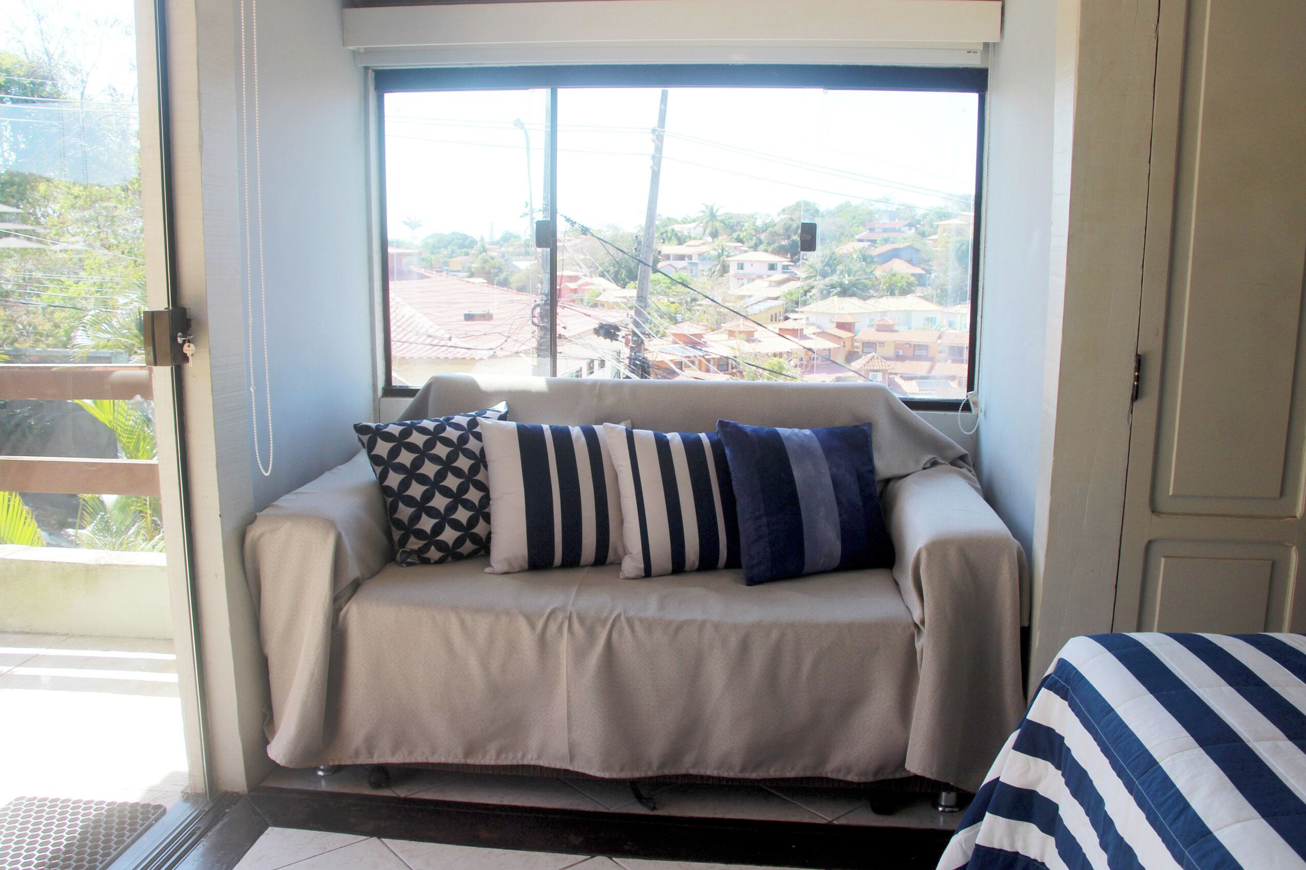 A room with a sofa near a window, a door, and a view of buildings outside.