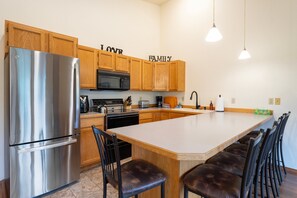 A kitchen with wooden cabinets, stainless steel appliances, a large island with bar stools, and pendant lighting.