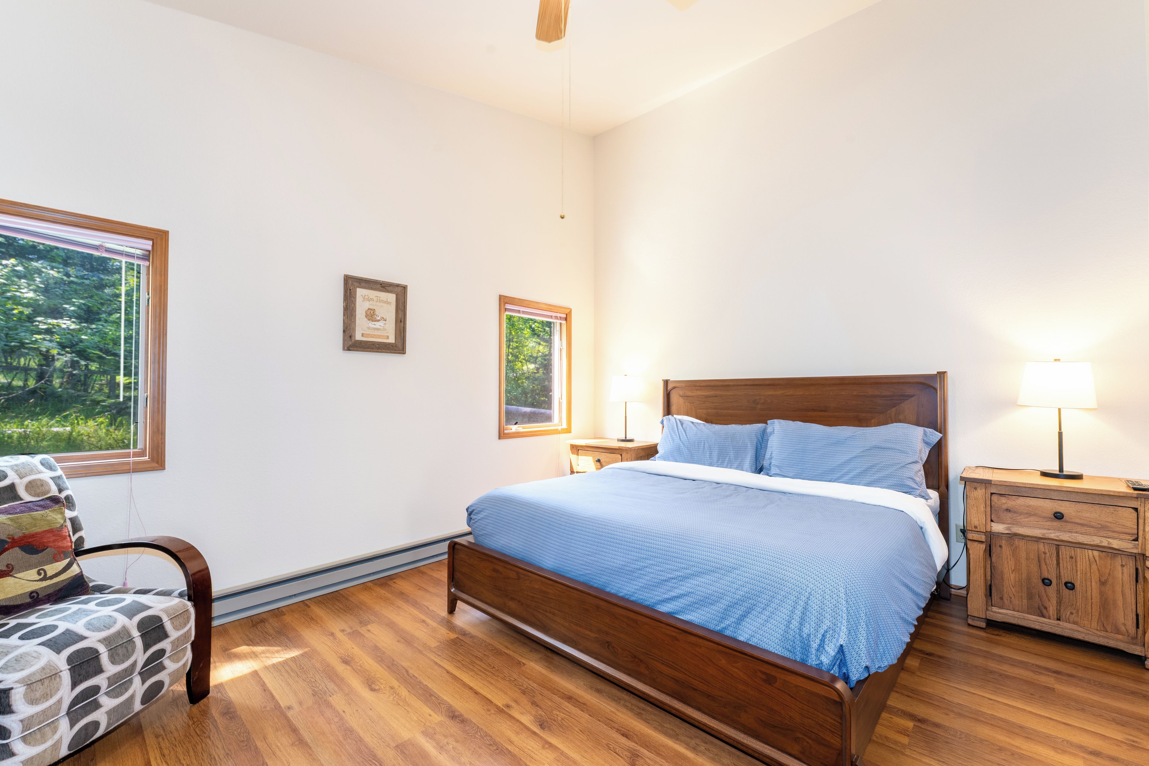 A bedroom with a wooden bed, a nightstand, a chair, and two windows.