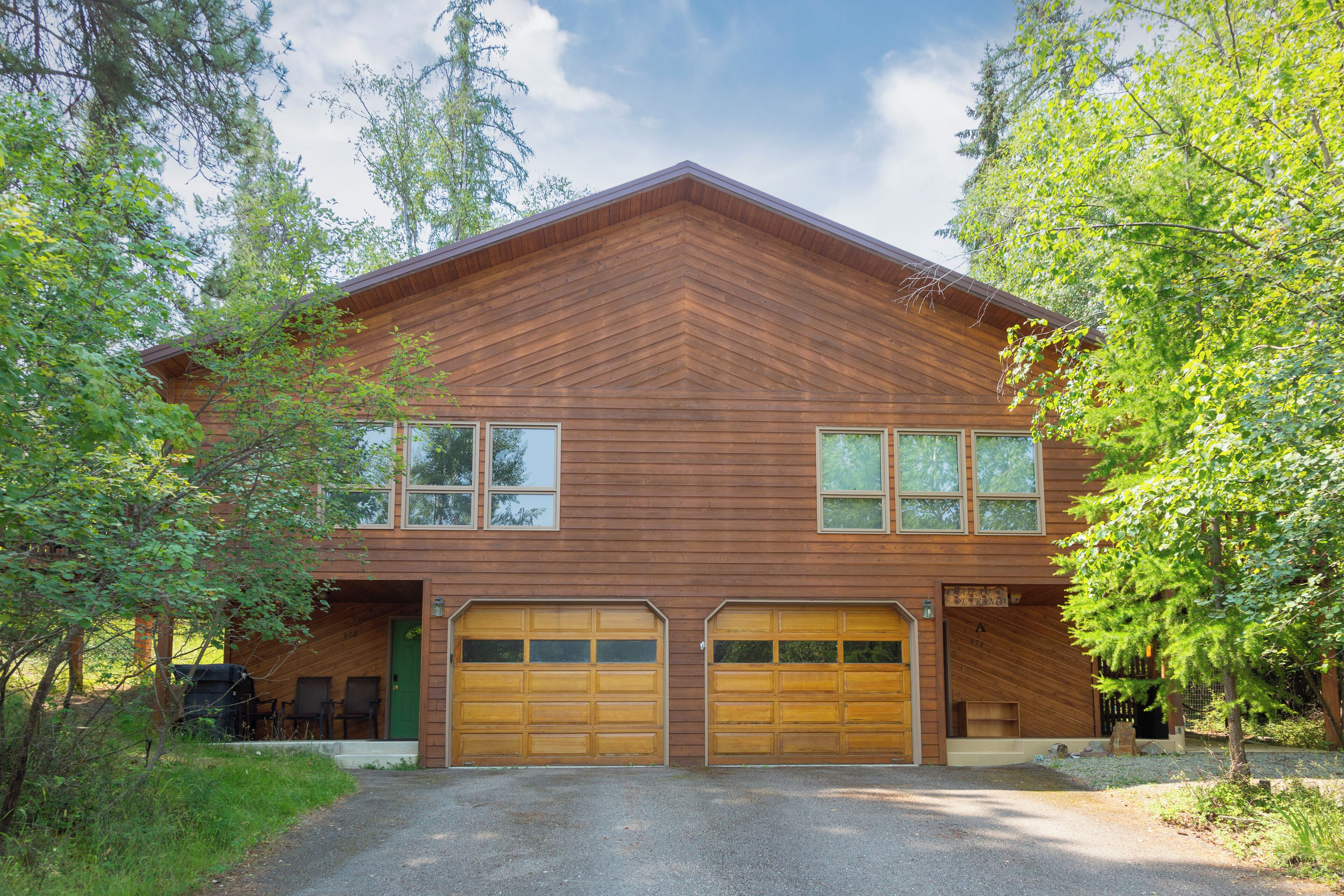 A two-story wooden house with a garage, surrounded by trees.