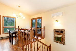 A dining area with a wooden table and chairs, a staircase with wooden railings, and a wall-mounted air conditioning unit.