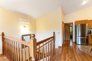 A wooden staircase with a handrail, a kitchen with a stainless steel refrigerator, and a wall-mounted air conditioner. - New Listing! Montana Ridgeline Retreat | GNP + Ski + Hike (Whitefish)