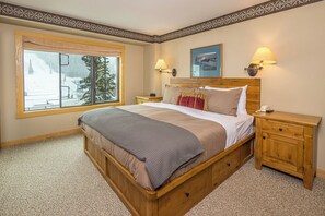 Une chambre avec une grande fenêtre, une tête de lit en bois, deux lampes de chevet et une table de nuit.