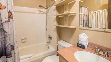 Un baño con bañera, inodoro, lavamanos y un espejo que refleja toallas.