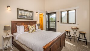 A bedroom with a large bed, bedside lamps, a framed picture, a door leading outside, and a window with a view.