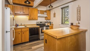 A kitchen with wooden cabinets, a stainless steel sink, a stove, and a wooden island.