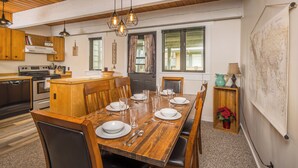 A dining area with a wooden table set for six, a kitchen in the background, and a world map on the wall.