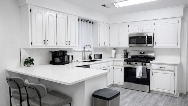 A modern kitchen with white cabinetry, a central island with bar stools, a built-in oven, a microwave, and a coffee maker. - Recently Updated, King bed, Near U of A & Downtown (Springdale)