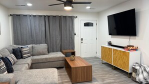 A living room with a sectional sofa, a wooden coffee table, a TV on the wall, and a door in the background. - Recently Updated, King bed, Near U of A & Downtown (Springdale)