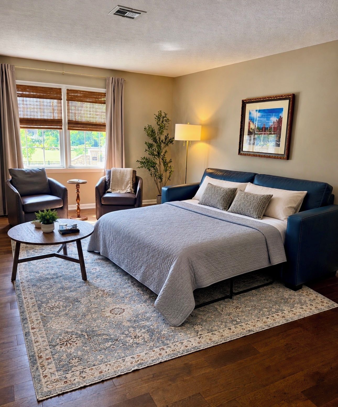 A bedroom with a bed, two armchairs, a side table, a lamp, a painting, and a window with curtains.