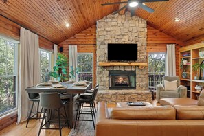 A cozy cabin interior with a stone fireplace, wooden ceiling, a dining area, and a comfortable seating area. - Cabin 6 Minutes From Silver Dollar City, Sleeps 6 (Branson)
