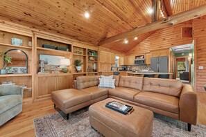 Ein geräumiges Wohnzimmer mit einer großen Ledersitzgruppe, Holzböden mit dekorativen Elementen und einer Küchenzeile mit modernen Geräten.