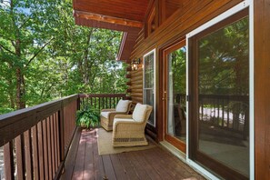 A wooden deck with two wicker chairs, a large sliding glass door, and a view of a forest. - Cabin 6 Minutes From Silver Dollar City, Sleeps 6 (Branson)