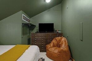 Ein Schlafzimmer mit einem Bett, einem braunen Ledersessel, einem Schminktisch, einem Fernseher und einem Schild an der Wand.
